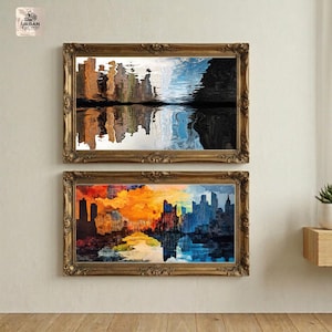 Puede incluir: Dos pinturas de paisajes urbanos abstractos enmarcadas. La pintura superior presenta tonos marrones, blancos, azules y negros, mientras que la pintura inferior muestra tonos naranjas, azules y amarillos. Ambas están en marcos dorados ornamentados.