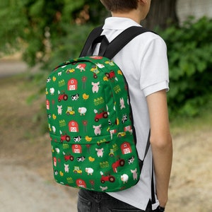 Könnte beinhalten: Ein grüner Rucksack mit einem Farmtier-Druck. Der Druck zeigt Schweine, Kühe, Hühner, Traktoren und Scheunen. Der Rucksack hat schwarze Träger und einen Reißverschluss.