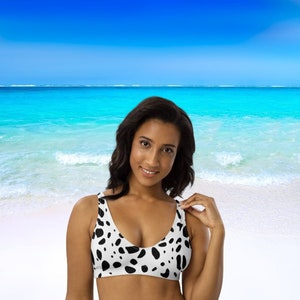 May include: A woman wearing a black and white spotted bikini top with a scoop neck.
