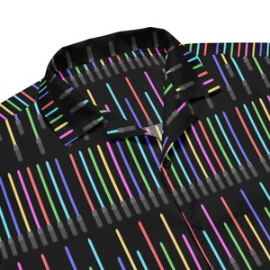 May include: A black button-up shirt with a repeating pattern of colorful lightsabers. The shirt has a classic collar and a button closure.