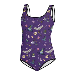 May include: Purple one-piece swimsuit with a black trim. The swimsuit has a pattern of various magical items, including a witch's hat, an owl, a wand, a book, and a crystal ball.
