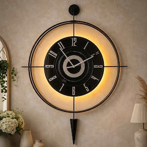 Puede incluir: Un reloj de pared grande y redondo con una esfera negra y números blancos. El reloj tiene un marco de metal negro con una luz cálida y brillante detrás de la esfera. Un péndulo negro cuelga debajo. El reloj está montado en una pared.
