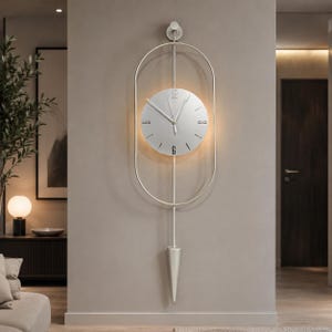 Peut inclure: Une horloge murale argentée dotée d'un cadran circulaire avec des index et des aiguilles noirs, encastrée dans un cadre métallique ovale vertical. L'horloge comprend une tige verticale centrale descendant vers un poids de pendule conique.