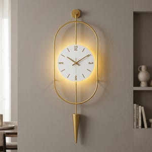 May include: A modern wall clock with a gold-colored frame and a white clock face. The clock has gold-colored hands and hour markers. The clock is approximately 24 inches tall and 12 inches wide. The clock is hanging on a gray wall.