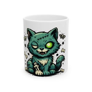 May include: White ceramic mug featuring a cartoon zombie cat with green fur, a stitched head, and a single green eye. The cat is holding a bone, with bones and butterflies scattered around it. A fun, spooky design.
