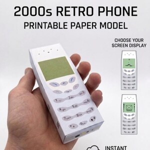 Könnte beinhalten: Ein weißes Papiermodell eines Retro-Telefons aus den 2000er Jahren wird in einer Hand gehalten. Das Telefon hat einen grünen Bildschirm und eine Tastatur mit Zahlen und Symbolen. Der Text "2000s RETRO PHONE PRINTABLE PAPER MODEL" steht oben. Das Bild enthält auch den Text "CHOOSE YOUR SCREEN DISPLAY" und "INSTANT DOWNLOAD PDF".