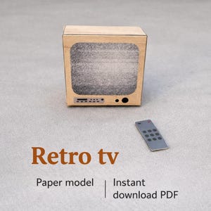 May include: A miniature retro TV paper model with a static screen, accompanied by a small remote control. The TV has a light brown frame and a series of buttons below the screen. Text on the image reads "Retro tv", "Paper model", and "Instant download PDF".