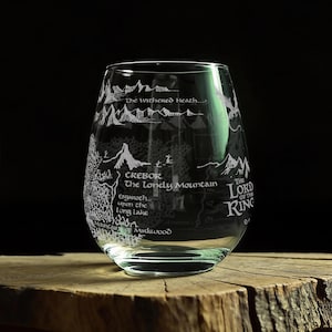 May include: A clear stemless wine glass featuring a white etched map design of Middle-earth. The glass displays text including The Withered Heath, Erebor, The Lonely Mountain, Esgaroth upon the Long Lake, Mountains of Mirkwood, and The Lord of the Rings.