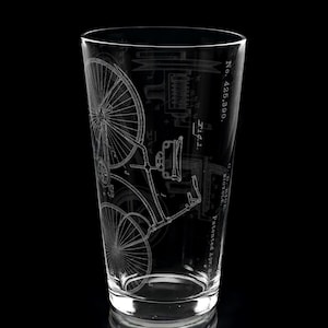 May include: A clear glass pint tumbler featuring a white etched technical drawing of a vintage bicycle. The design includes the text No. 425,390, Fig 1, and O.D. Rice, Bicycle, Patented Apr. 8, 1890, displayed vertically along the side of the glass.