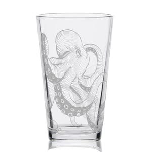May include: A clear glass with a detailed etched design of an octopus. The octopus is depicted with its tentacles wrapping around the glass. The glass is a standard pint glass shape.