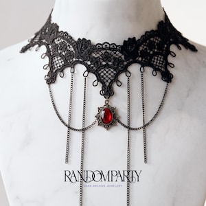 May include: Black lace choker necklace with a red gemstone pendant and dangling chains. The choker features intricate floral lace detailing and the text "RANDOMPARTY DARK ARCHIVE JEWELRY".