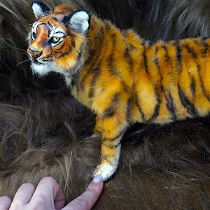 May include: A handcrafted tiger figurine featuring a vibrant orange coat with distinct black stripes, white fur accents on the face and paws, and detailed facial features including yellow eyes, pointed ears, and a textured, realistic appearance.