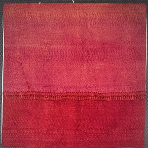 May include: A square textile piece featuring a two-tone red color scheme with a subtle herringbone weave pattern. The upper section is a lighter shade of red, while the lower section is a deeper red, separated by a horizontal stitched seam.