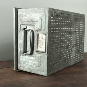 May include: A rectangular galvanised metal storage bin featuring a perforated side panel, a sturdy metal handle on the front face, and a small rectangular label holder containing a white insert with the handwritten black text 4.22.