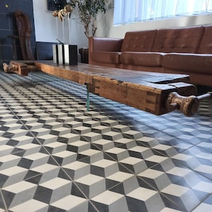 Könnte beinhalten: Eine lange, rechteckige Werkbank, die als Couchtisch umfunktioniert wurde, mit einer dicken, verwitterten braunen Holzplatte mit sichtbaren Schwalbenschwanzverbindungen und zwei großen, manuell bedienbaren Holzschraubstöcken an den Enden, auf dünnen Metallbeinen.