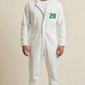 May include: White jumpsuit with a collared neckline and long sleeves. The jumpsuit features a green number "28" patch on the chest. The garment has a zipper closure and a fitted waist. The model is wearing a white t-shirt underneath.