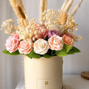 May include: A cylindrical beige gift box containing an arrangement of artificial roses in shades of pink, peach, white, and purple, accented with dried pampas grass and baby's breath. The box features a gold rectangular label with the text Flowers For You.