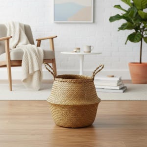 Peut inclure: Un panier de rangement beige tissé avec des poignées en corde. Le panier a une base évasée et un sommet cylindrique. Il est posé sur un sol en bois. L'arrière-plan comprend une chaise, une petite table et une plante en pot. Hauteur du panier : environ 30 cm.