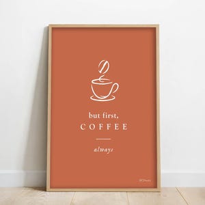 Peut inclure: Tableau encadré avec un fond orange brûlé. L'œuvre présente une illustration blanche d'une tasse et d'un grain de café, avec les mots "but first, COFFEE always" dans une police épurée et moderne. Le cadre est de couleur bois clair.