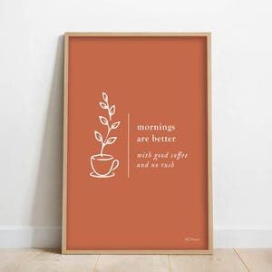 Peut inclure: Impression d'art encadrée avec un fond terracotta. L'impression présente un dessin au trait blanc d'une tasse à café avec une plante et le texte "mornings are better with good coffee and no rush."