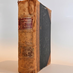 May include: An antique book with a worn, tan leather cover and a black spine. The title "A Romanized Dictionary of Chinese" is visible on a red label. The book shows signs of age and wear.