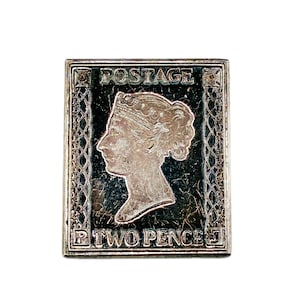 Könnte beinhalten: Eine rechteckige Metallbrosche mit einem erhabenen, silberfarbenen Profil von Königin Victoria vor einem dunklen, strukturierten Hintergrund. Das Wort POSTAGE steht oben und TWO PENCE unten, flankiert von den Buchstaben P und J in den Ecken.