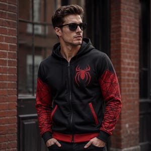 May include: Black zip-up hoodie with red accents and a spider emblem on the chest. The sleeves feature a red web design. The hoodie has a red trim on the pockets and bottom hem.