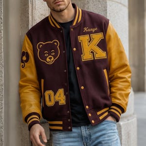 Puede incluir: Chaqueta universitaria granate y dorada con mangas de cuero. La chaqueta presenta el nombre "Kanye" y la letra "K" en dorado, junto con un gr&aacute;fico de oso y el n&uacute;mero "04".