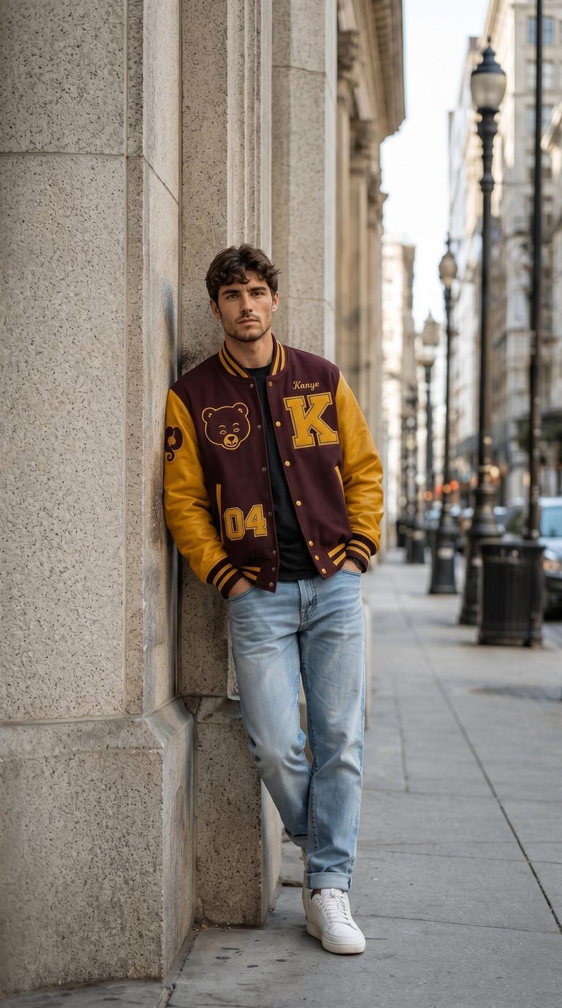 Puede incluir: Una chaqueta universitaria granate y dorada con el nombre "Kanye" y la letra "K" en la parte delantera. La chaqueta tambi&eacute;n presenta un gr&aacute;fico de oso y el n&uacute;mero "04". La persona lleva una camiseta negra, vaqueros azul claro y zapatillas blancas.