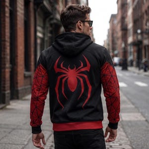 May include: Black hooded sweatshirt with a large red spider emblem on the back. The sleeves are red with a geometric pattern. The sweatshirt has a red trim at the bottom and around the hood.