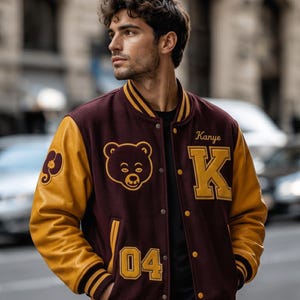 Puede incluir: Chaqueta universitaria granate y dorada con un logotipo de oso y el nombre "Kanye" y la letra "K" en dorado. La chaqueta tiene mangas doradas y el n&uacute;mero "04" en la parte delantera.