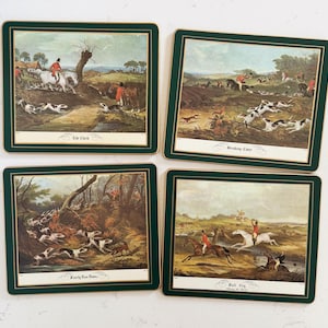 May include: Set of four square coasters with hunting scenes. Each coaster features a different vintage illustration with a green border and gold trim. The coasters depict riders on horseback, hounds, and rural landscapes.