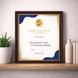 May include: A framed certificate with a dark brown wooden frame. The certificate has a gold border and features the text "CERTIFICATE OF ACHIEVEMENT" and "has achieved 3 Years of Continuous Sobriety". Decorative blue accents are present.