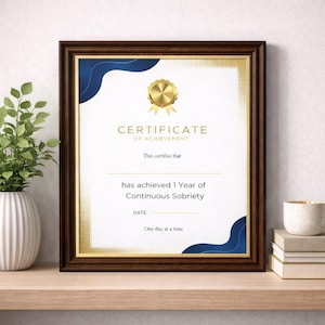 Puede incluir: Un certificado enmarcado con un sello dorado y detalles azules. El certificado dice "CERTIFICADO DE LOGRO" y "ha logrado 1 año de sobriedad continua". El marco es de color marrón oscuro.