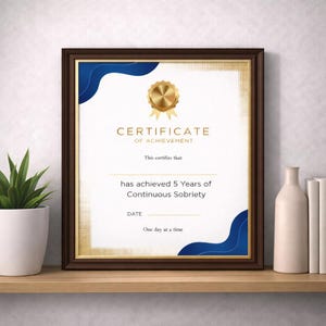 Może przedstawiać: Oprawiony certyfikat ze złotymi akcentami i niebieskimi elementami. Certyfikat głosi „CERTIFICATE OF ACHIEVEMENT” i potwierdza „5 lat ciągłej trzeźwości”. Rama jest ciemnobrązowa, a certyfikat jest wyświetlany na drewnianej półce.