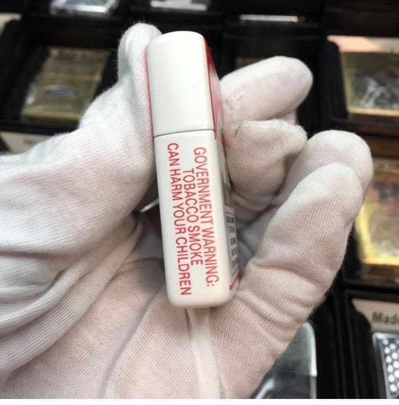 May include: A white and red rectangular object with the text "GOVERNMENT WARNING: TOBACCO SMOKE CAN HARM YOUR CHILDREN." The object is held in a gloved hand. The top of the object is white.