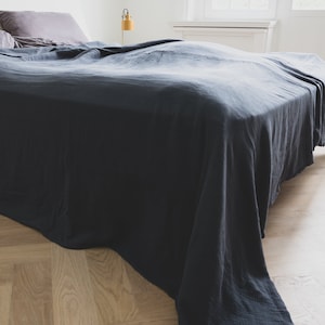 Könnte beinhalten: Eine dunkelblaue Tagesdecke bedeckt ein Bett, mit einem Kissen am Kopfende. Die Tagesdecke hat ein strukturiertes Aussehen und drapiert über die Seiten des Bettes. Der Raum hat ein minimalistisches Design mit Holzboden.