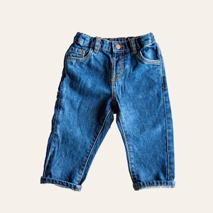 Può includere: Un paio di jeans blu in denim con chiusura a bottone e passanti per la cintura.