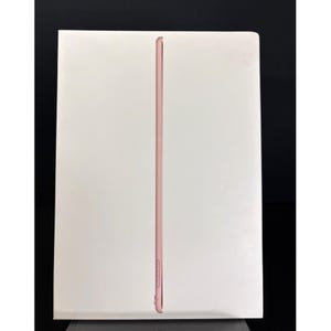 Può includere: Un tablet color oro rosa è presentato verticalmente, incorniciato da un bordo bianco. Il profilo laterale del tablet è visibile, evidenziando il suo design sottile e la disposizione dei pulsanti. Lo sfondo è una superficie bianca.