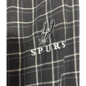 May include: A close-up of a black and white checked fabric with the word "SPURS" embroidered in white. The Spurs logo, a stylized spur and star, is also embroidered in white.