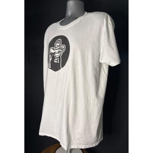 May include: White t-shirt with a black graphic of a basketball player in a circle, with the number 21 visible. The shirt has a crew neck and short sleeves. The shirt is displayed on a mannequin.
