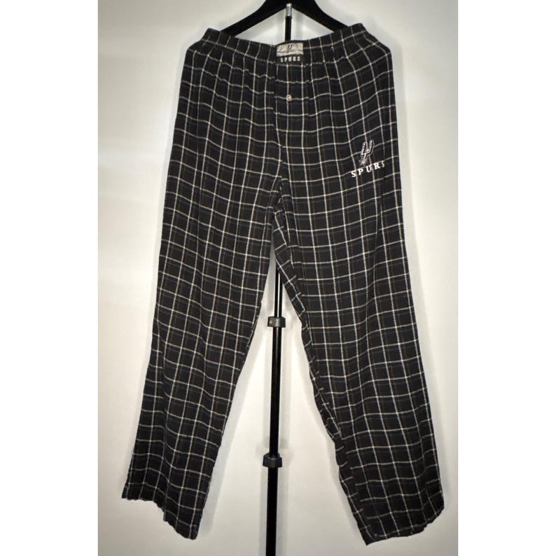 May include: Black and white checked pajama trousers with a button fastening and a small embroidered "SPURS" logo. The trousers are suspended on a black hanger against a white backdrop.