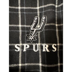 May include: Black and white checked fabric with an embroidered San Antonio Spurs logo and the word "SPURS" in white. The logo features a silver spur and a star.