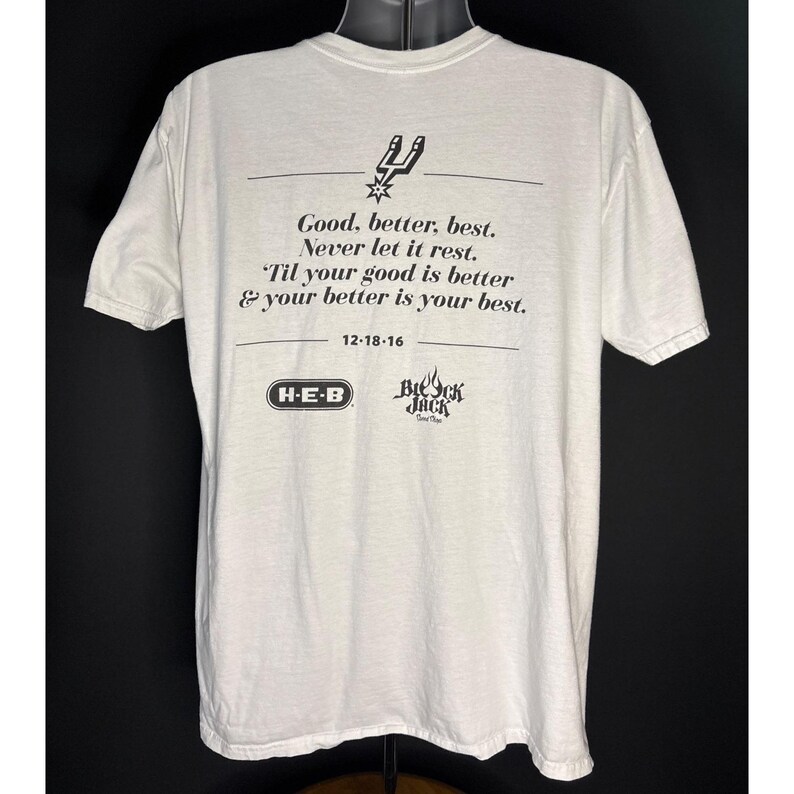May include: Off-white t-shirt featuring the text "Good, better, best. Never let it rest. 'Til your good is better & your better is your best." with the date 12-18-16. The shirt also has the logos of H-E-B and Breck Jack.
