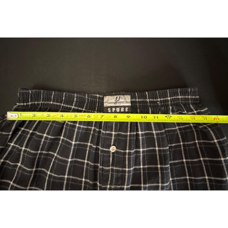 May include: Black and white plaid boxer shorts with a button closure. The waistband has the word "SPURS" printed on it. The shorts measure approximately 30 cm across.