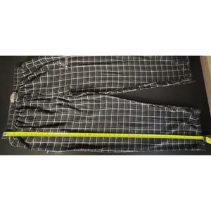 May include: Black and white checked pajama trousers with an elasticated waistband. The trousers have a white grid pattern over a black background. A yellow measuring tape is laid across the trousers. The trousers have the word "SPORTS" printed on them.