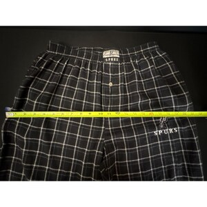 May include: Black and white plaid pajama trousers with the San Antonio Spurs logo embroidered on the leg. The trousers have a button closure and an elastic waistband. The trousers measure approximately 30 cm across the waist.