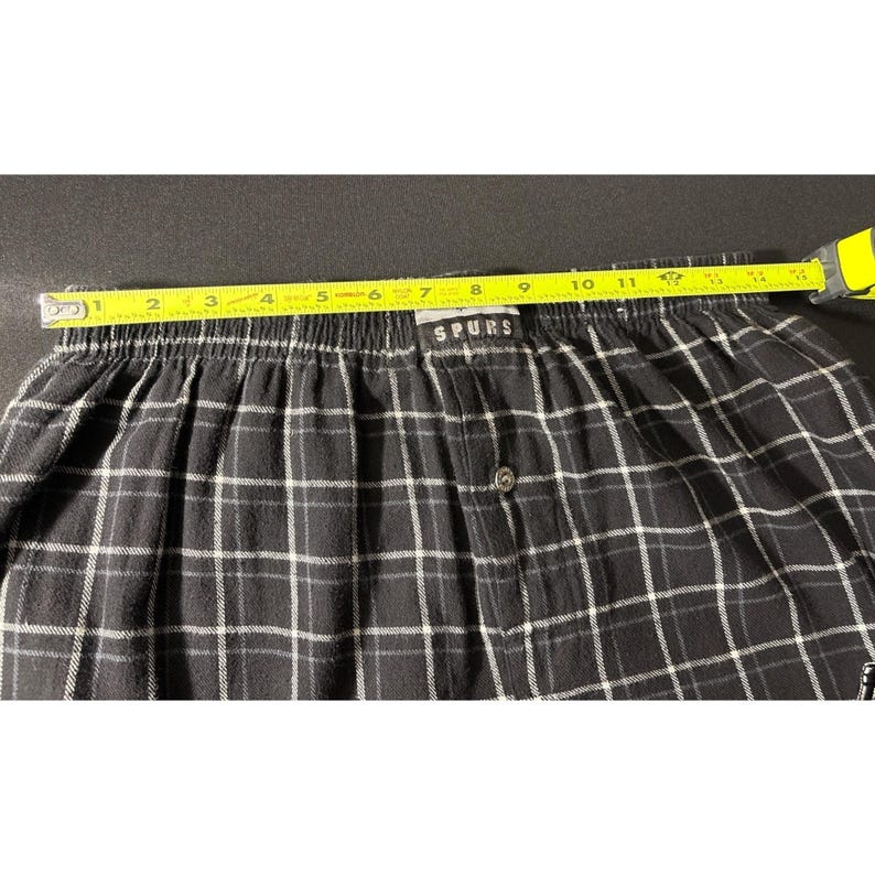 May include: Black and white plaid boxer shorts with the word "SPURS" on the waistband. The shorts are measured with a yellow tape measure, showing a length of approximately 28 cm.