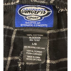 May include: A close-up of a Concepts Sport sleepwear label. The blue label features white text and a logo, stating "SLEEPWEAR BYCOLLEGE CONCEPTS" and "100% COTTON/ALGODON". The label is attached to black and white checked fabric.