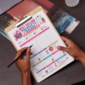 May include: A wooden clipboard holding a Best Selling Products Tracker sheet with colorful graphics, including a shopping cart, trophy, and pie chart. The document features sections for tracking sales, top-performing products, and goals, with pink and teal accents.